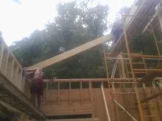 Carpenter raising a rafter beam on a new second story frame in Clinton