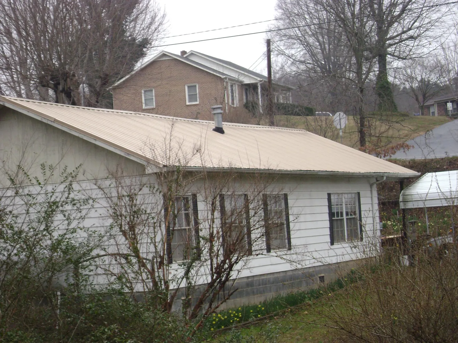 Tan metal roof on a white sided house set into a hillside — Commercial Roofing by Roofing Brothers in Clinton